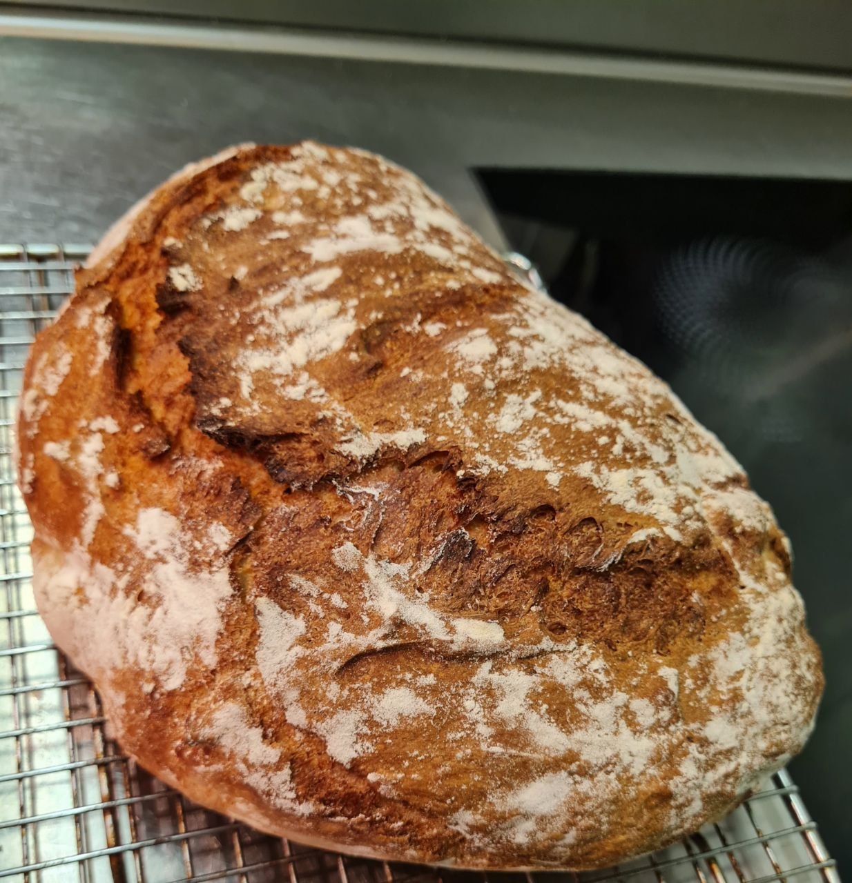 A rustic loaf of homemade bread with a floured, deeply caramelised crust.