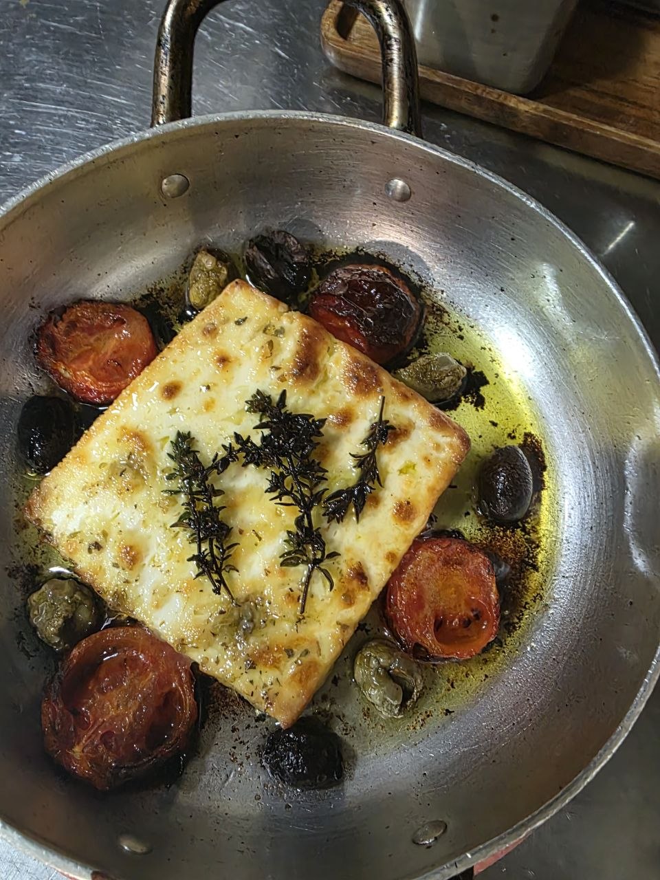 Baked feta with roasted cherry tomatoes, black olives, capers and thyme, served in the pan.