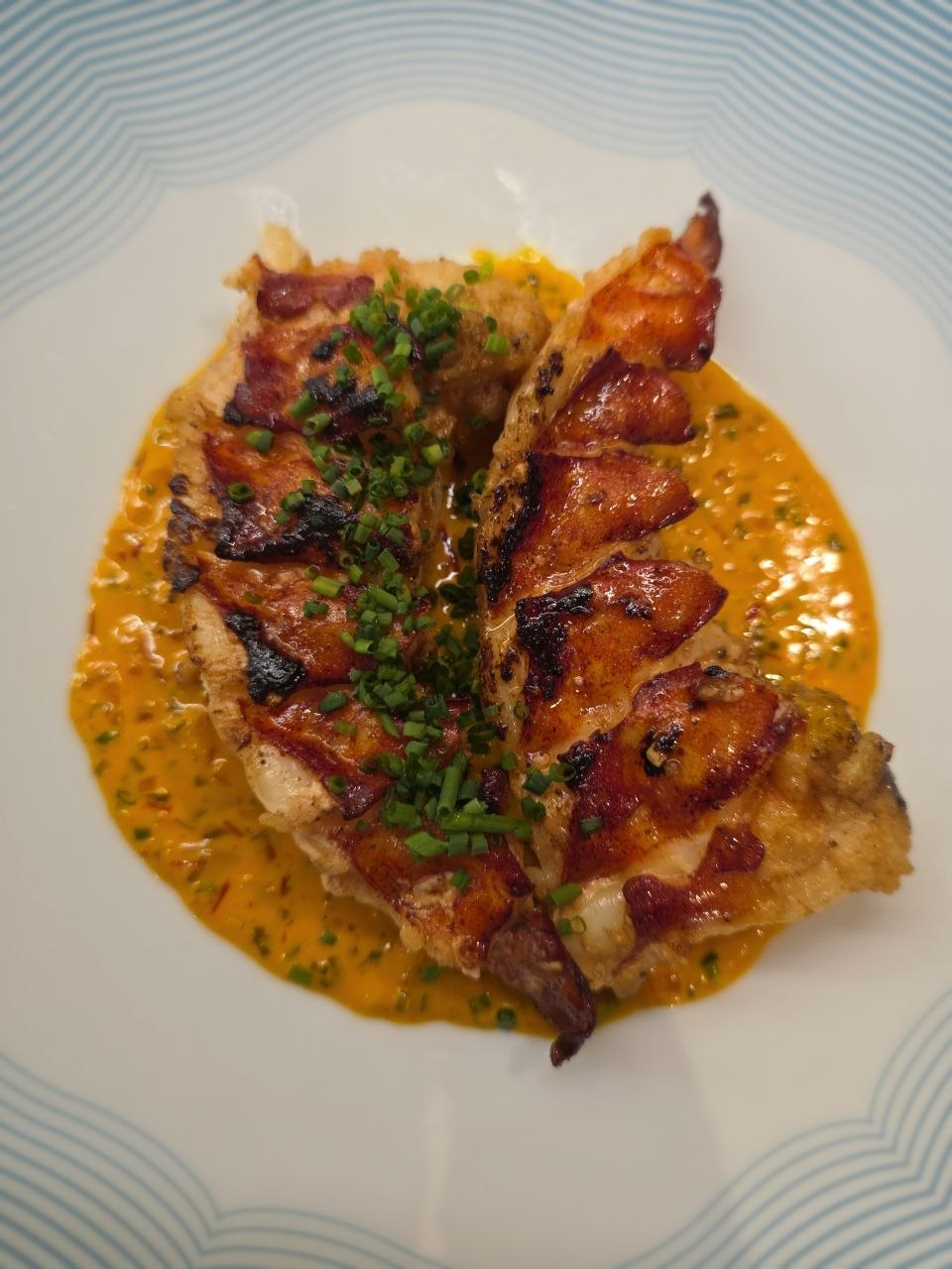 Two grilled lobster tails on a saffron sauce, finished with chopped chives.