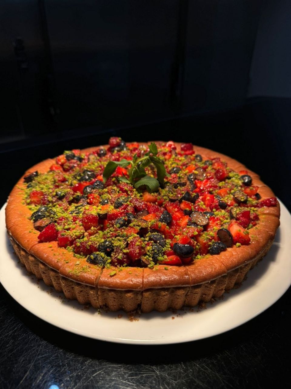 A whole New York cheesecake topped with strawberries, blueberries, raspberries, crushed pistachio and mint.