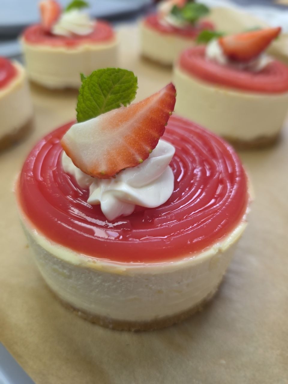 An individual cheesecake with a glossy strawberry glaze, whipped cream, a fresh strawberry and mint.