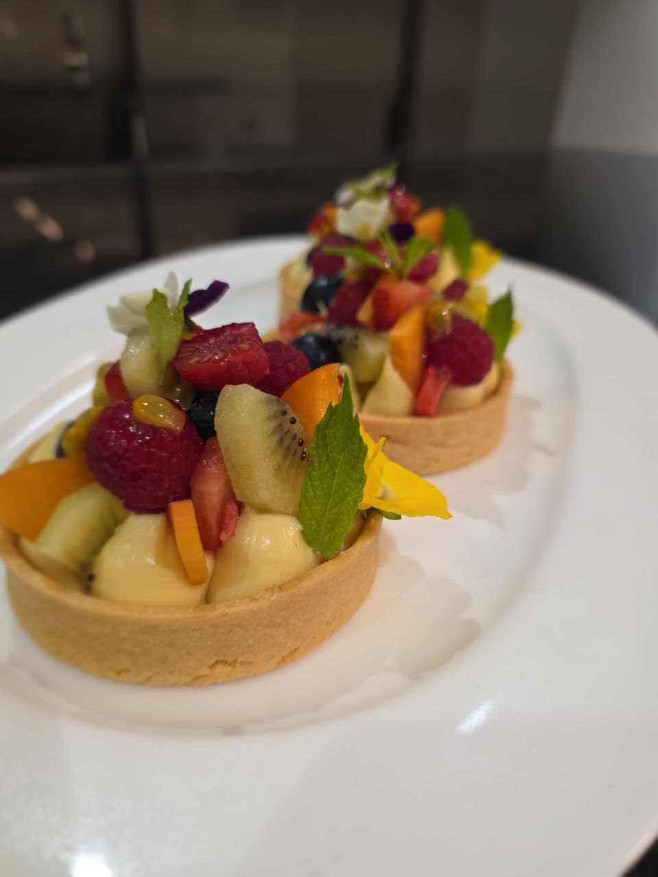 Sablé tarts with vanilla crème pâtissière, topped with seasonal fruit and edible flowers, on a white plate.