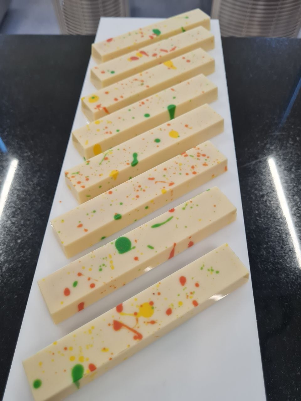 A row of white chocolate Piña Colada bars splashed with coloured cocoa butter, on a long white platter.
